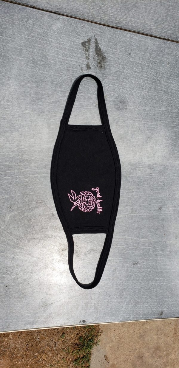 handmade fair trade black face mask with a soft pink screen printed design on the right-hand side of the mask of a chrysanthemum with the text, "good health" above it in cursive.