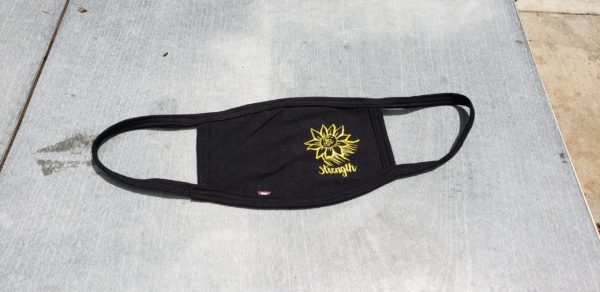 handmade fair trade black face mask with a yellow, screen printed design on the right-hand side of the mask of a sunflower with the word, "Strength" below it in cursive.