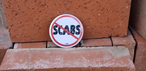 White Button with Red "No-Symbol" across degraded text reading, "SCABS" resting on stacked bricks