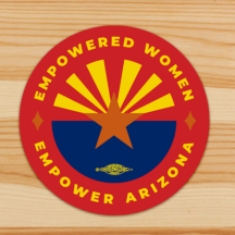 a round sticker sitting on a piece of wood. The sticker has a centered the arizona state flag with a union bug on the bottom. The text around the flag and along the inner circle is (top) "empowered women" (bottom) "empower women".